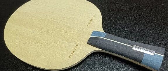 Yinhe inner carbon blade lying flat on a dark surface, showing the blade face and handle