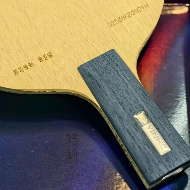 Table tennis blade showing Yinhe branding with rubber attached, resting on a colorful background