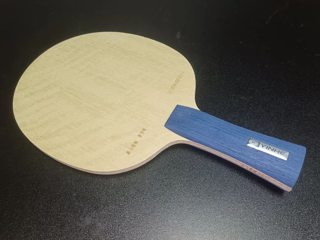 A single Yinhe table tennis blade with blue handle on a dark surface