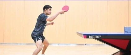 Kanak Jha demonstrating his parallel-feet forehand loop stance at a Butterfly table in a training facility