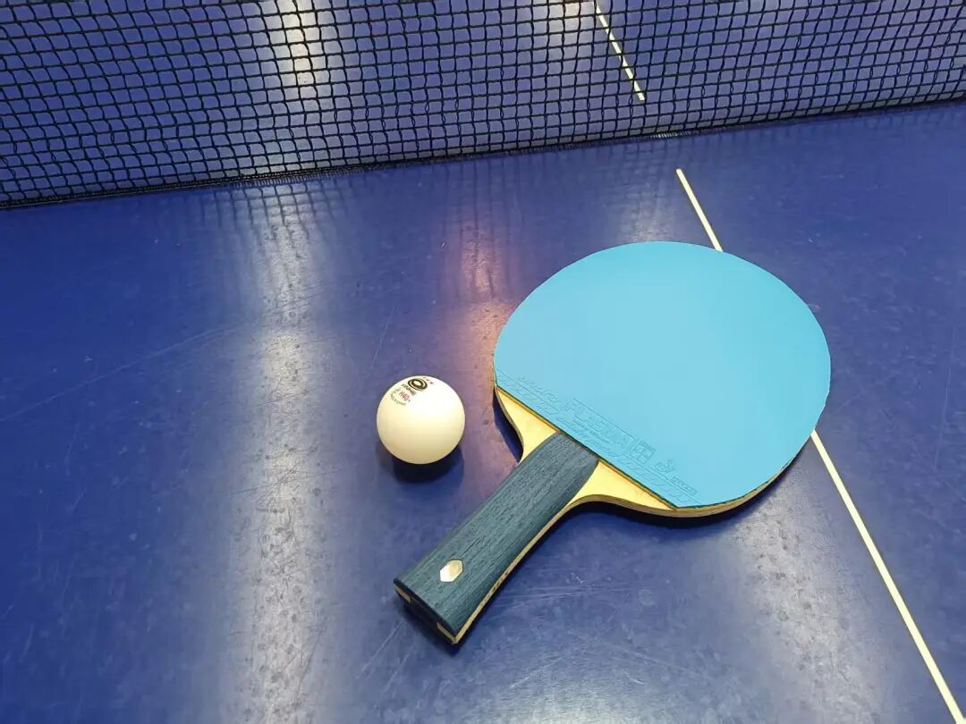 Penhold paddle with blue rubber and a table tennis ball resting on a blue court surface