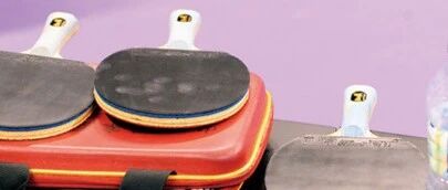 Three table tennis paddles resting on a red equipment case courtside
