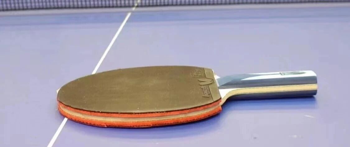A table tennis paddle with Butterfly Tenergy rubber lying on a blue table next to the net