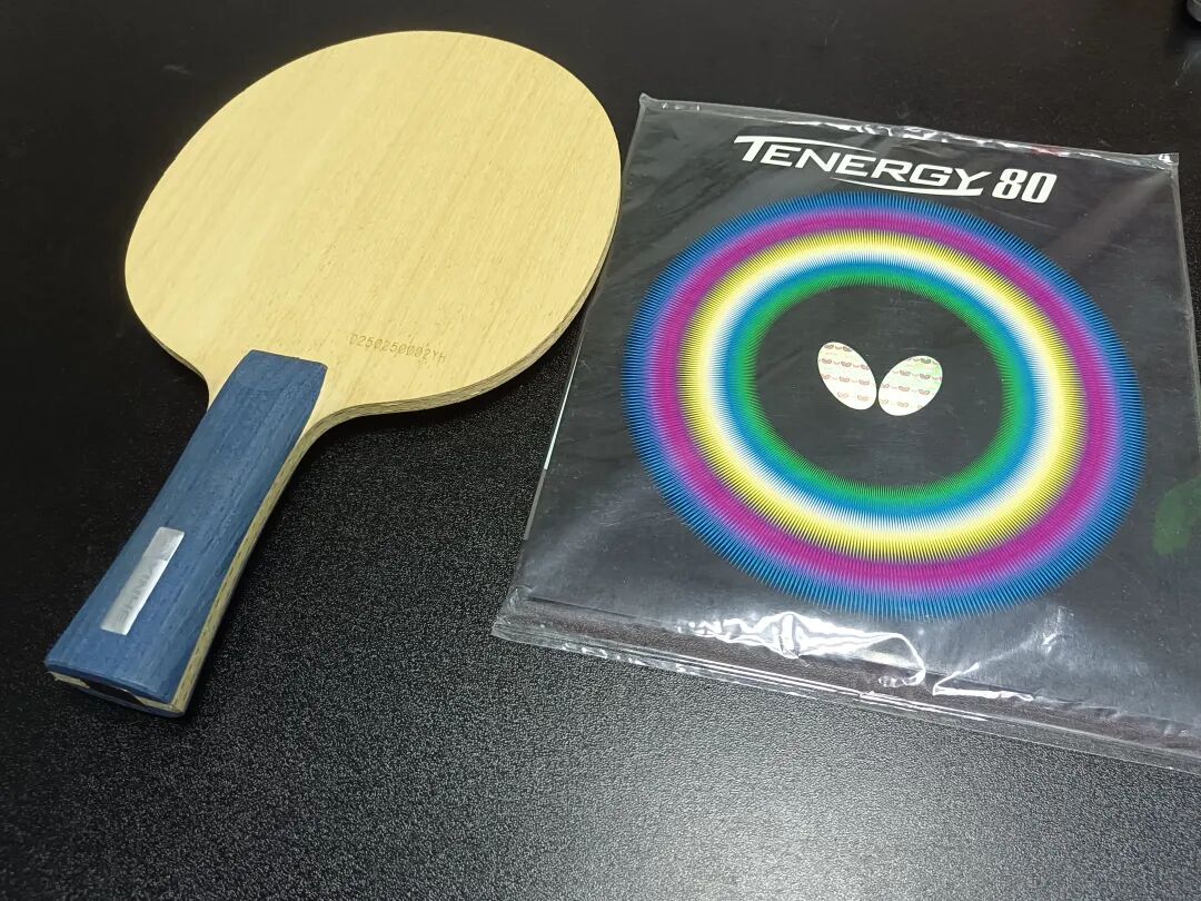 A table tennis blade next to a Butterfly Tenergy 80 rubber package
