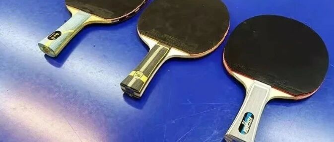 Three table tennis paddles with dark rubber sheets resting on a blue table surface