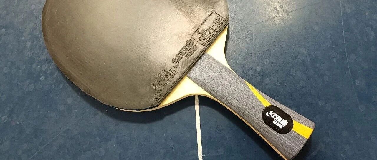 DHS table tennis blade with Hurricane 3 rubber mounted, lying on a blue table surface