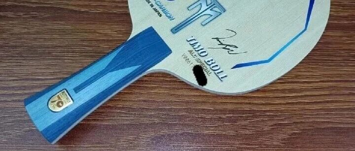 Timo Boll ALC 70th Anniversary blade with blue handle resting on a wooden table, showing the blade face