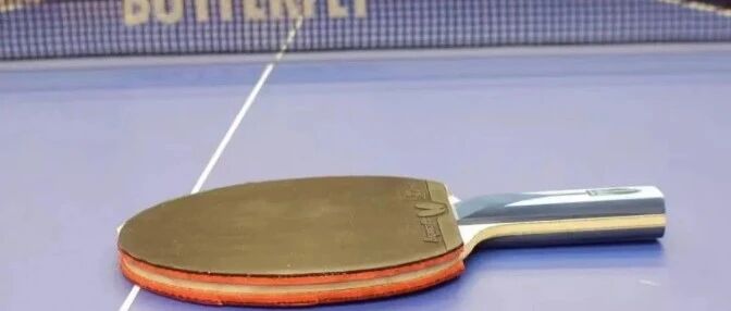 A table tennis paddle lying face-down on a blue Butterfly table, net visible in the background