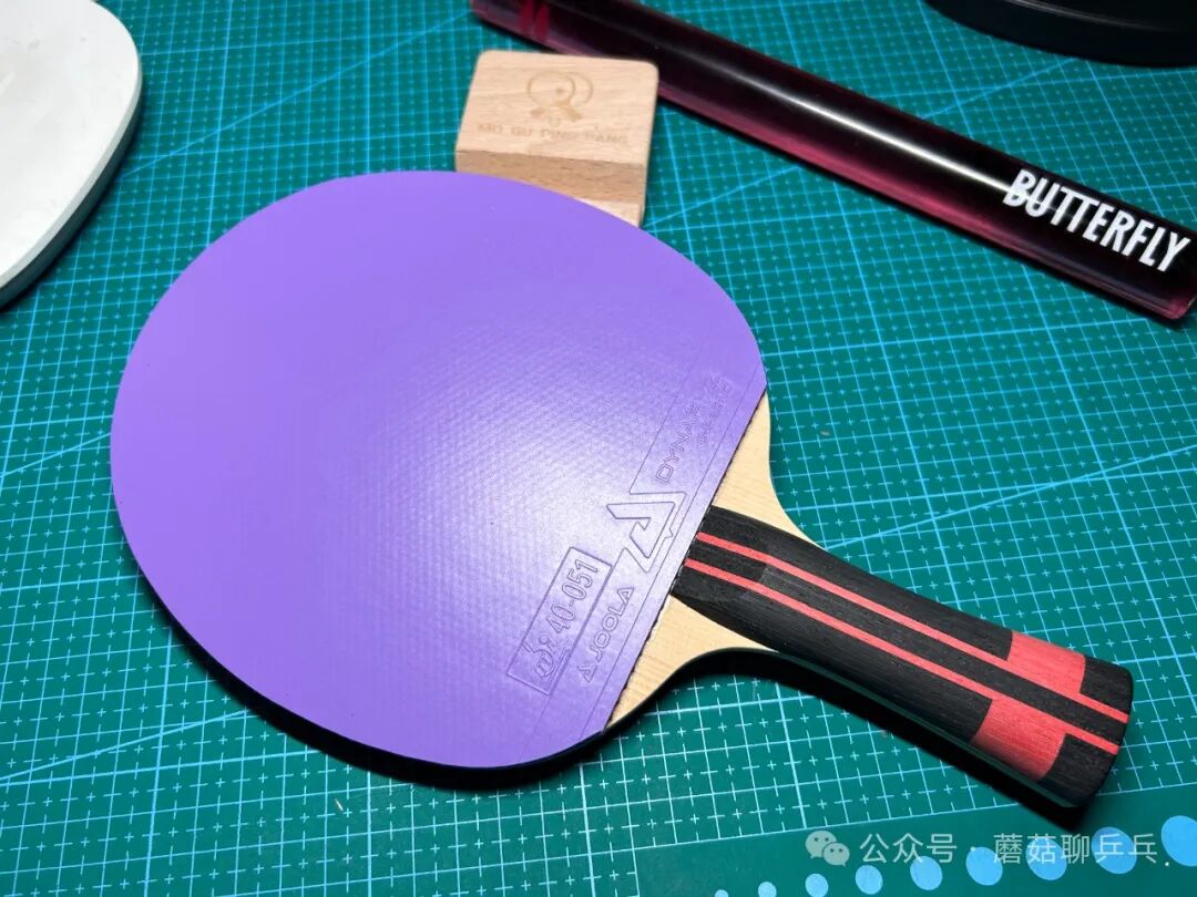 Joola Dynaryz Inferno purple rubber sheet on a paddle beside a Butterfly case