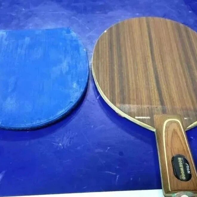 Xu Xin's Rosewood 5 penhold blade (brown walnut grain) on a blue mat, with a rubber sheet alongside
