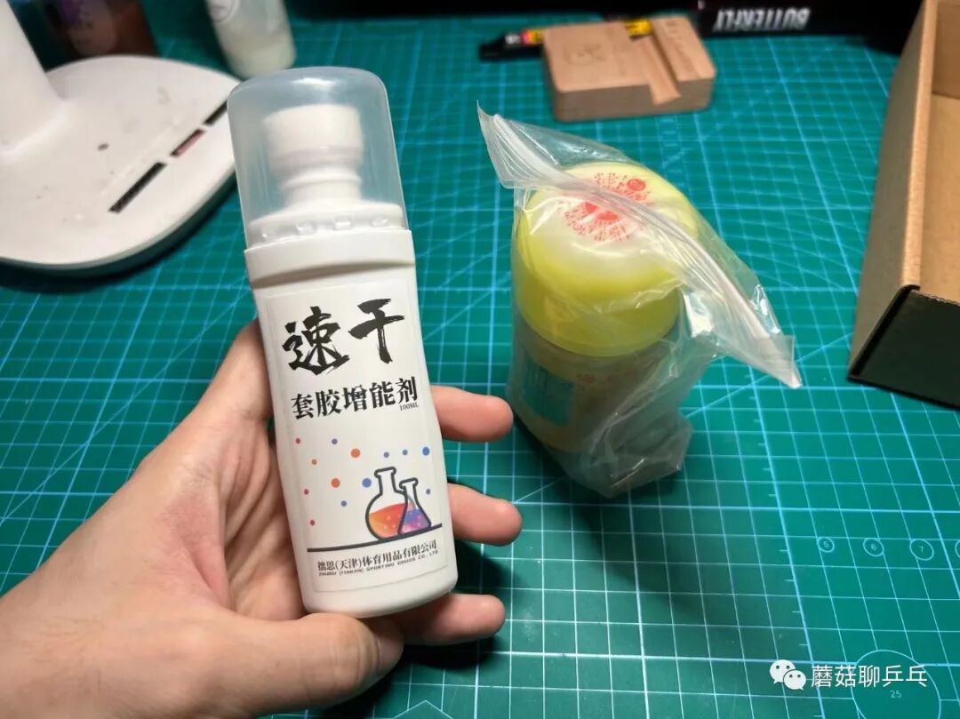 Hand holding a bottle of Pinyi quick-dry rubber booster oil next to a table tennis rubber sheet on a cutting mat