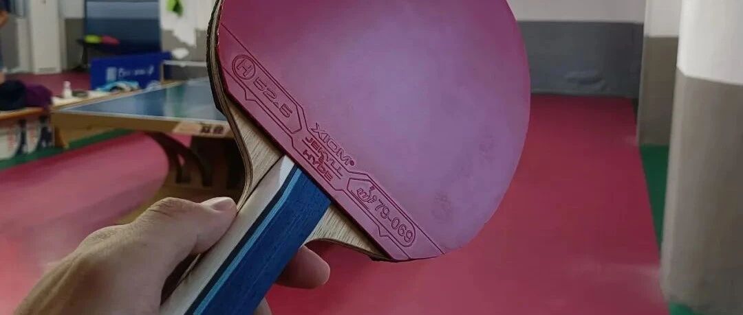 A player holding a paddle with a pink XIOM Jekyll and Hyde rubber at an indoor training hall