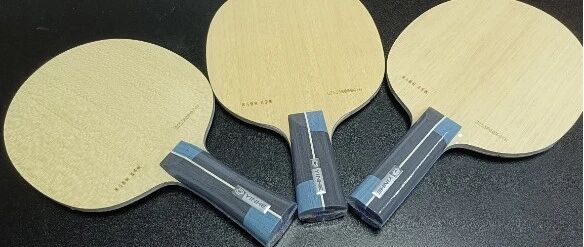 Three Yinhe table tennis blades lined up on a dark surface showing the handle and face