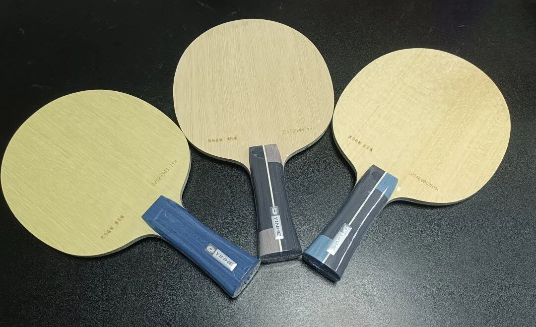 Two table tennis blades on a dark surface with blue grip wrapping