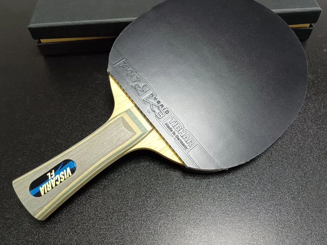 A table tennis paddle with black inverted rubber and purple handle on a blue table