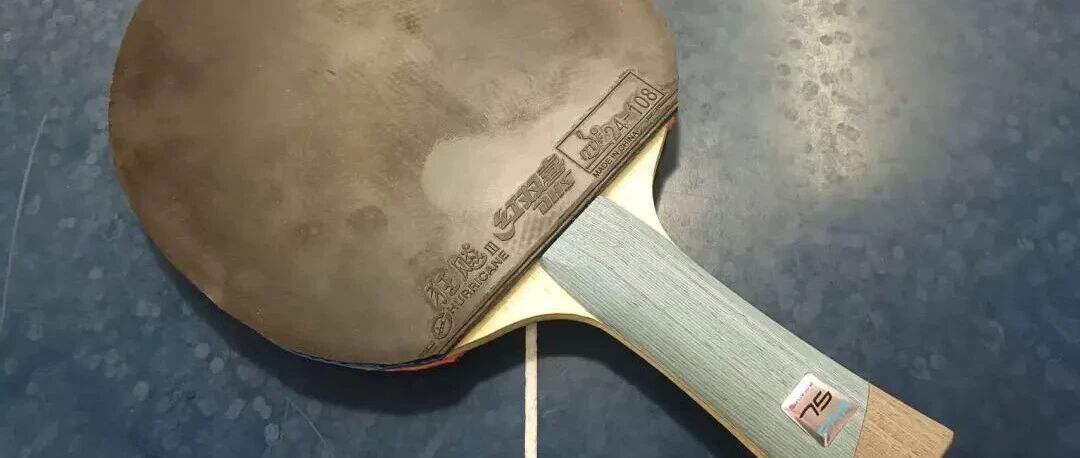 A table tennis racket with Hurricane 3 rubber and a gray blade on a blue table surface