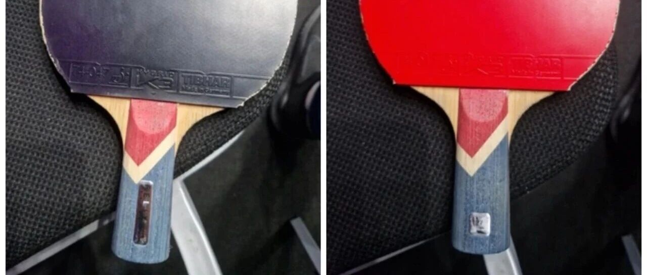 Penhold table tennis racket showing both black and red rubber sides, held against a dark surface