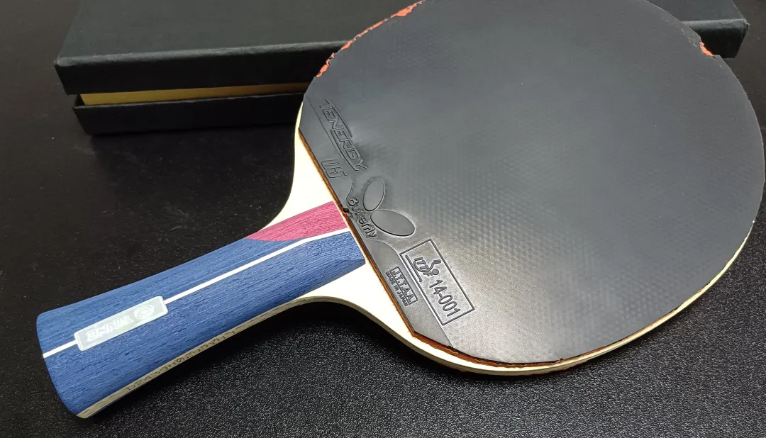 Table tennis racket assembled with a Tibhar blade and red rubber, resting against a Butterfly box