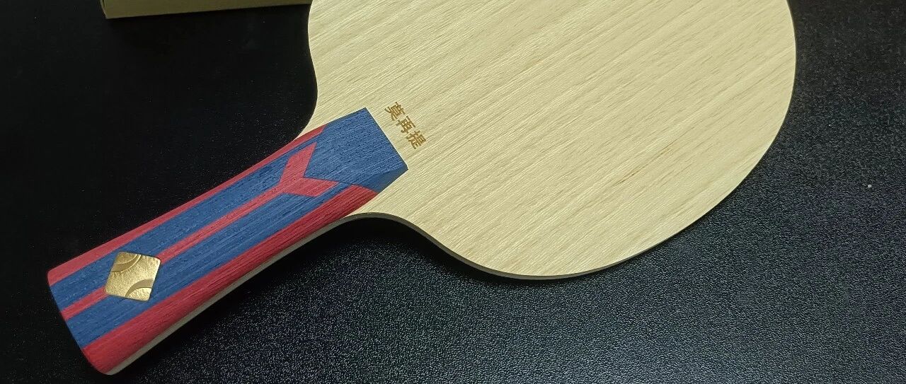 A custom table tennis blade with colorful handle resting on a black surface