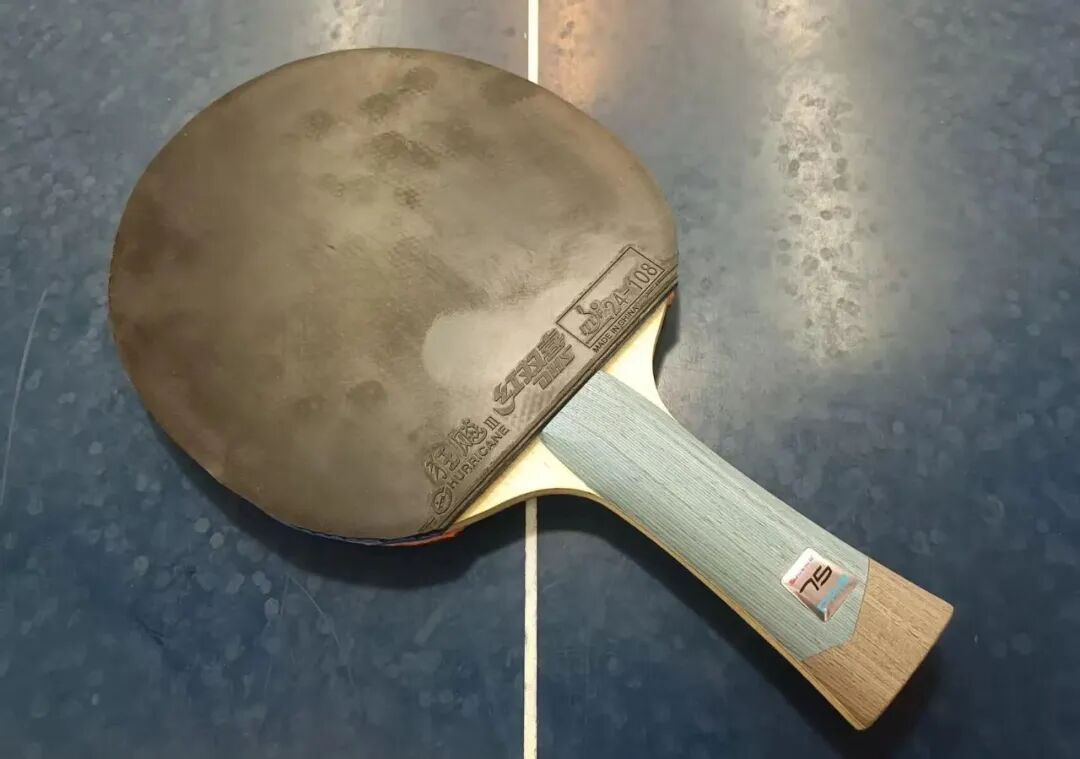 A table tennis blade with Hurricane 3 rubber mounted on a blue table surface