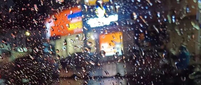 Rainy night city street viewed through a rain-streaked car windshield, atmospheric mood shot