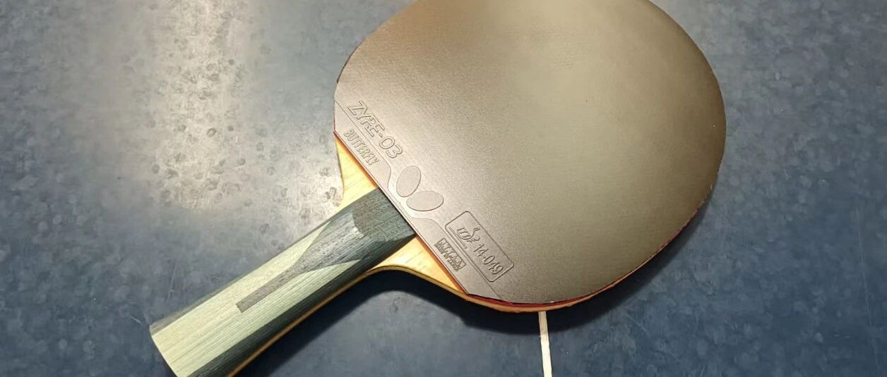 Table tennis paddle with Butterfly ZYRE-03 rubber on a blue court surface