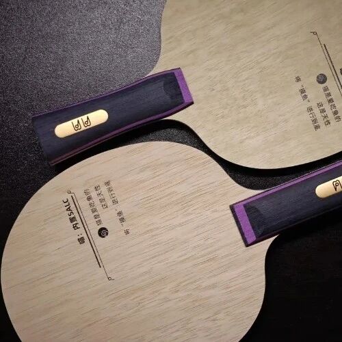 Two premium table tennis blades with dark wood grain and ornate handles displayed on a dark surface
