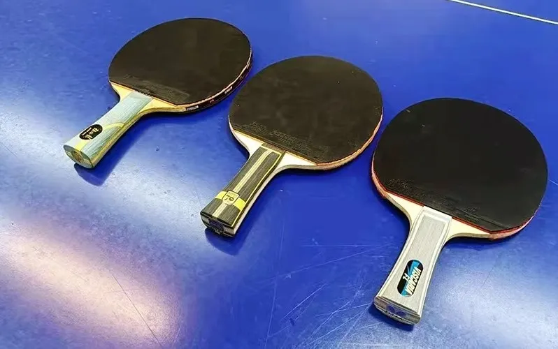 Multiple table tennis blades with rubbers attached showing different outer and inner carbon setups