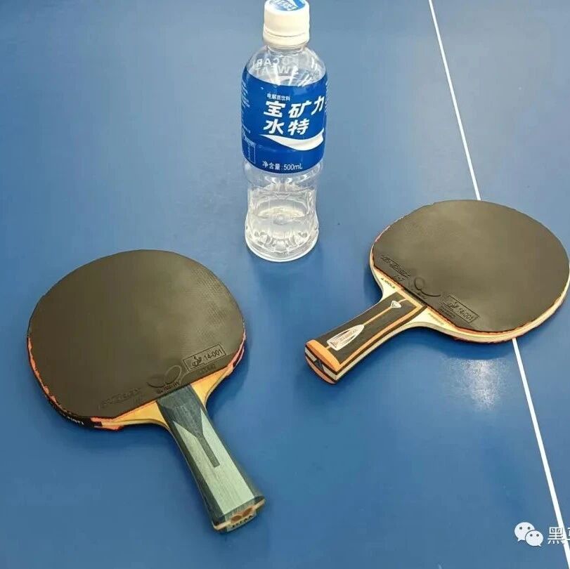 Two table tennis paddles and a sports drink bottle on a blue table